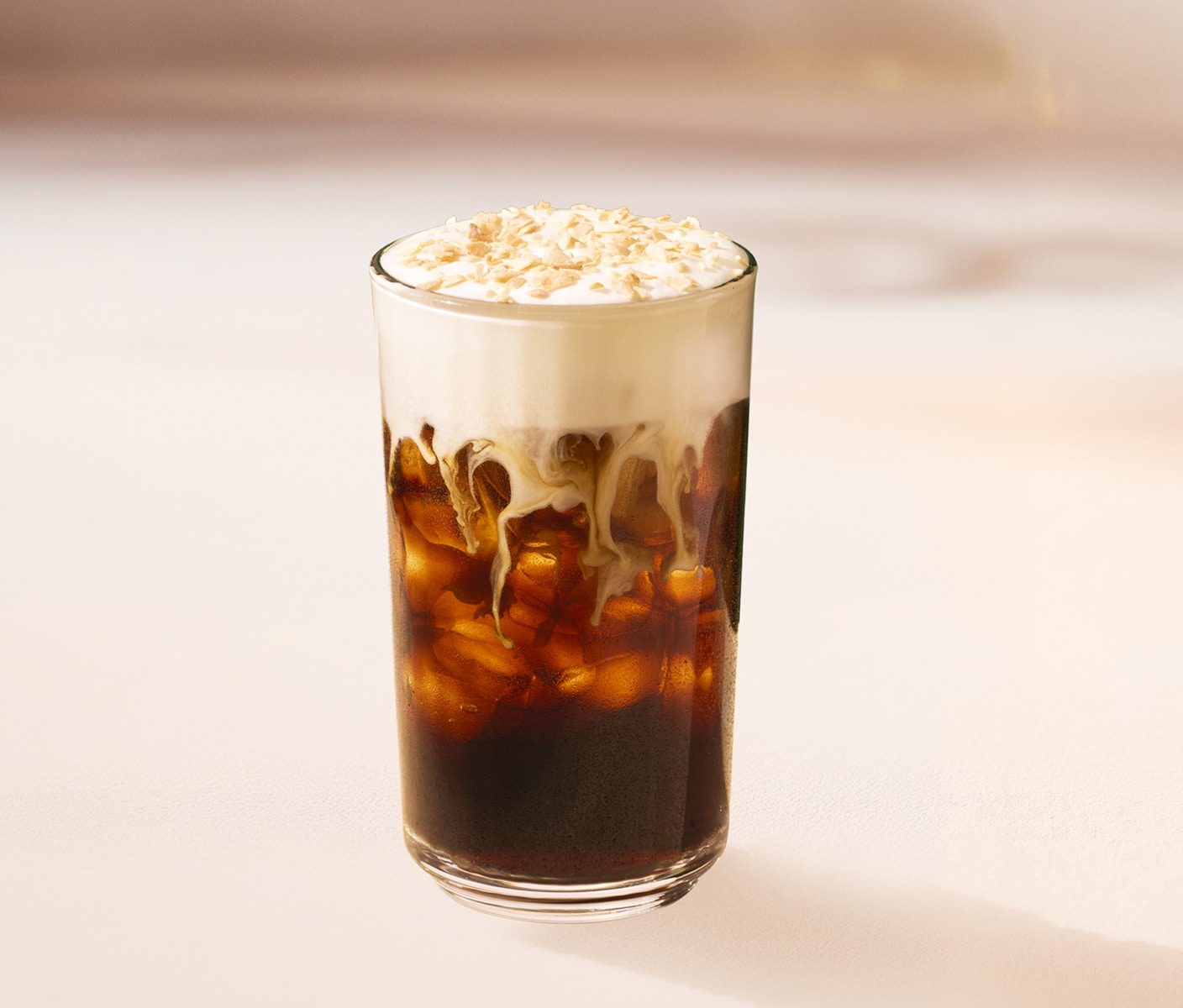 An iced coffee drink with a thick and cascading foam top in a glass.