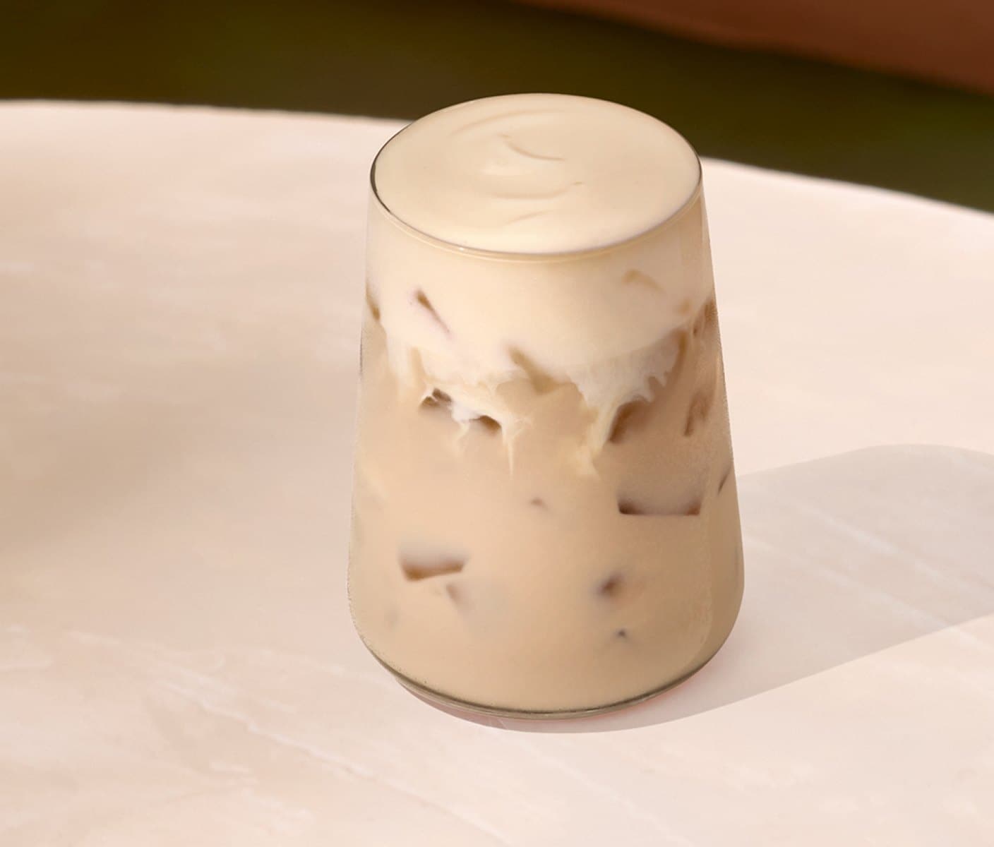 A creamy iced tea drink with a thick foam topping in a glass.