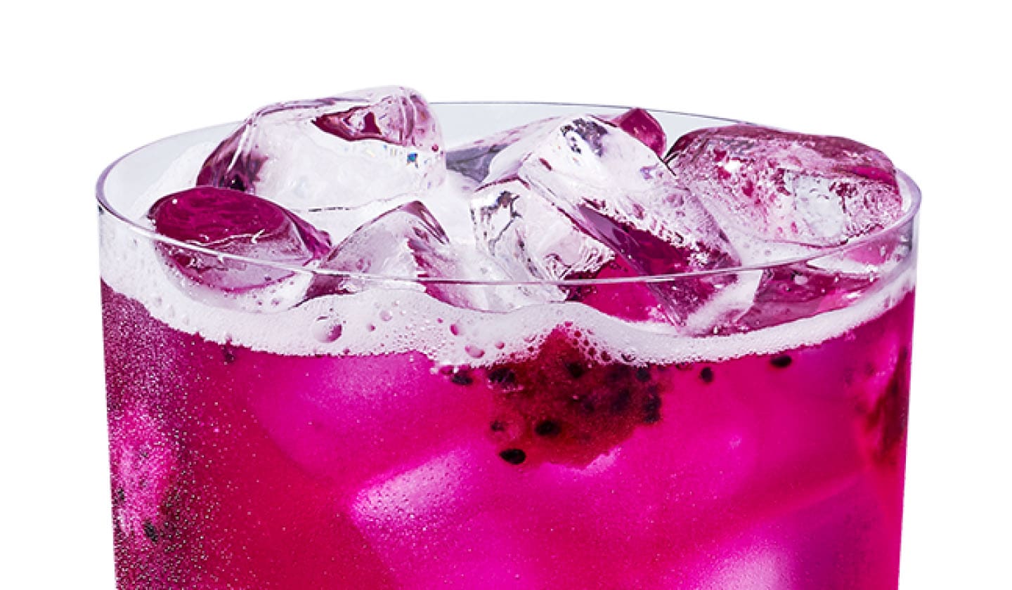 Close up of an iced mango and dragonfruit flavored drink with dragonfruit pieces in a glass.