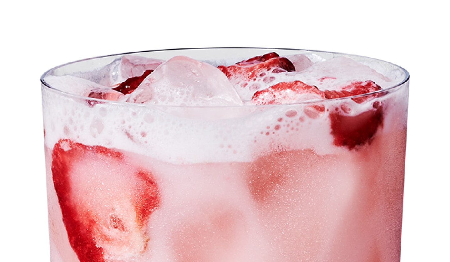 Close up of an iced strawberry flavored drink with coconutmilk and strawberry pieces in a glass.
