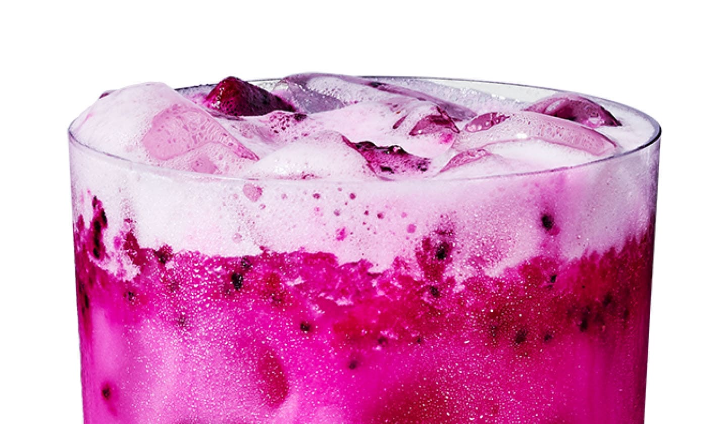 Close up of an iced mango and dragonfruit flavored drink with coconutmilk and dragonfruit pieces in a glass.
