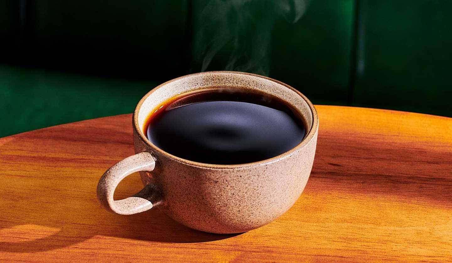 A stone mug filled with hot coffee on a wooden table.