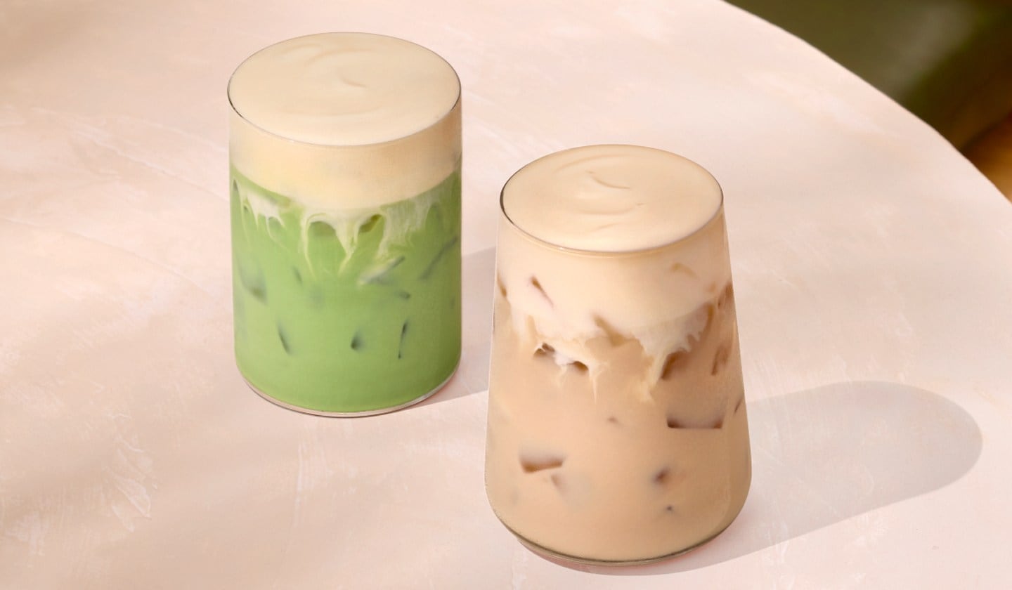 Two creamy iced tea drinks with thick foamy tops in glasses.