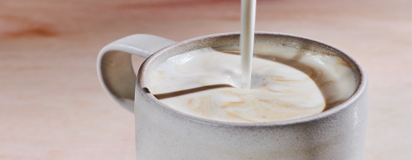 A hot coffee drink with steamed milk being poured into its foamy top.