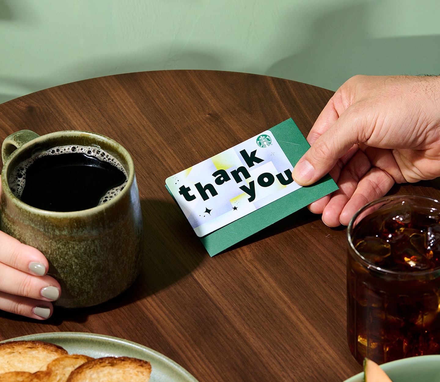 Close-up of two hands at a table. Someone is presenting a Thank You gift card to another person holding a coffee mug.