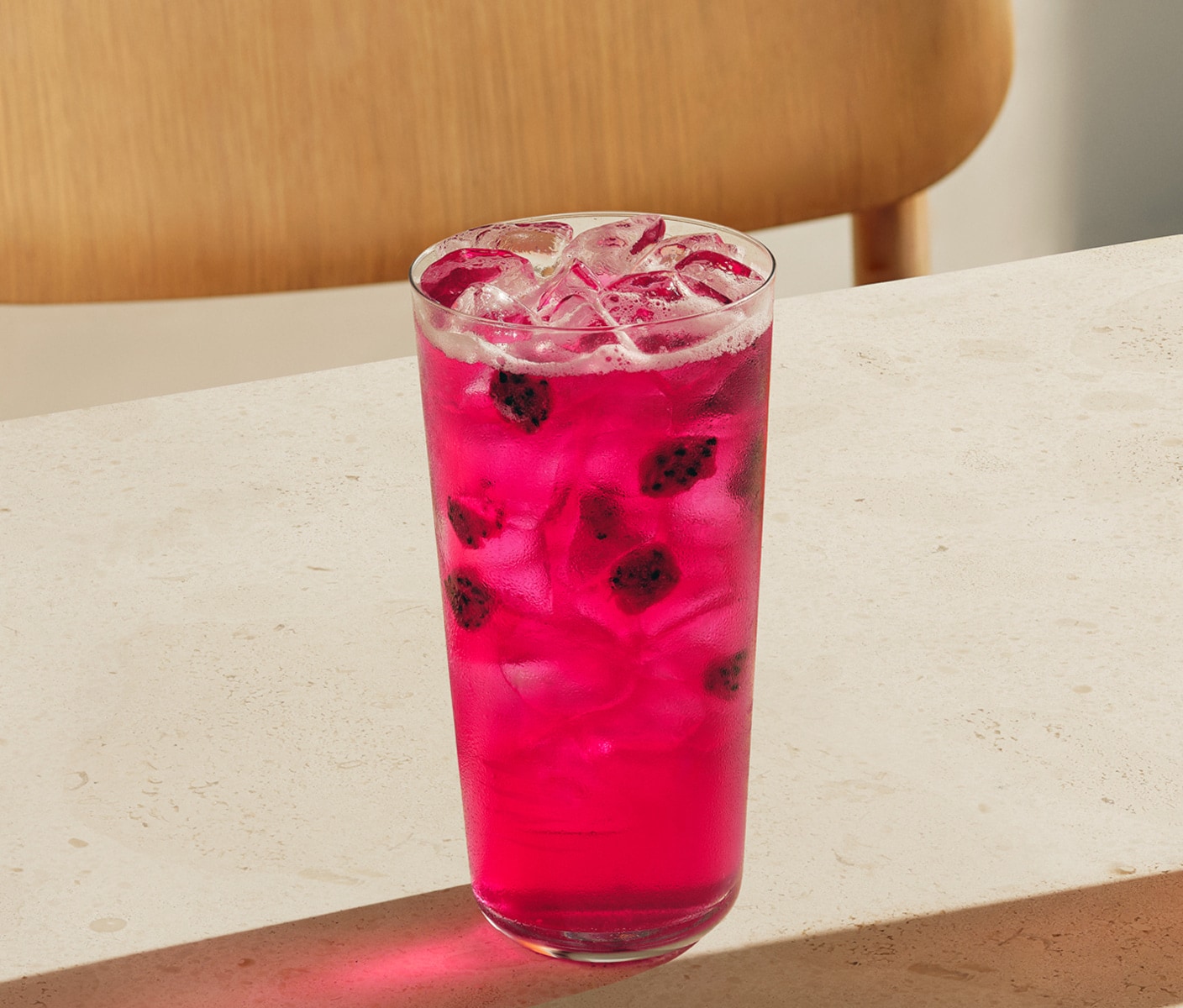 A bright iced beverage with pieces of dragonfruit in a glass.
