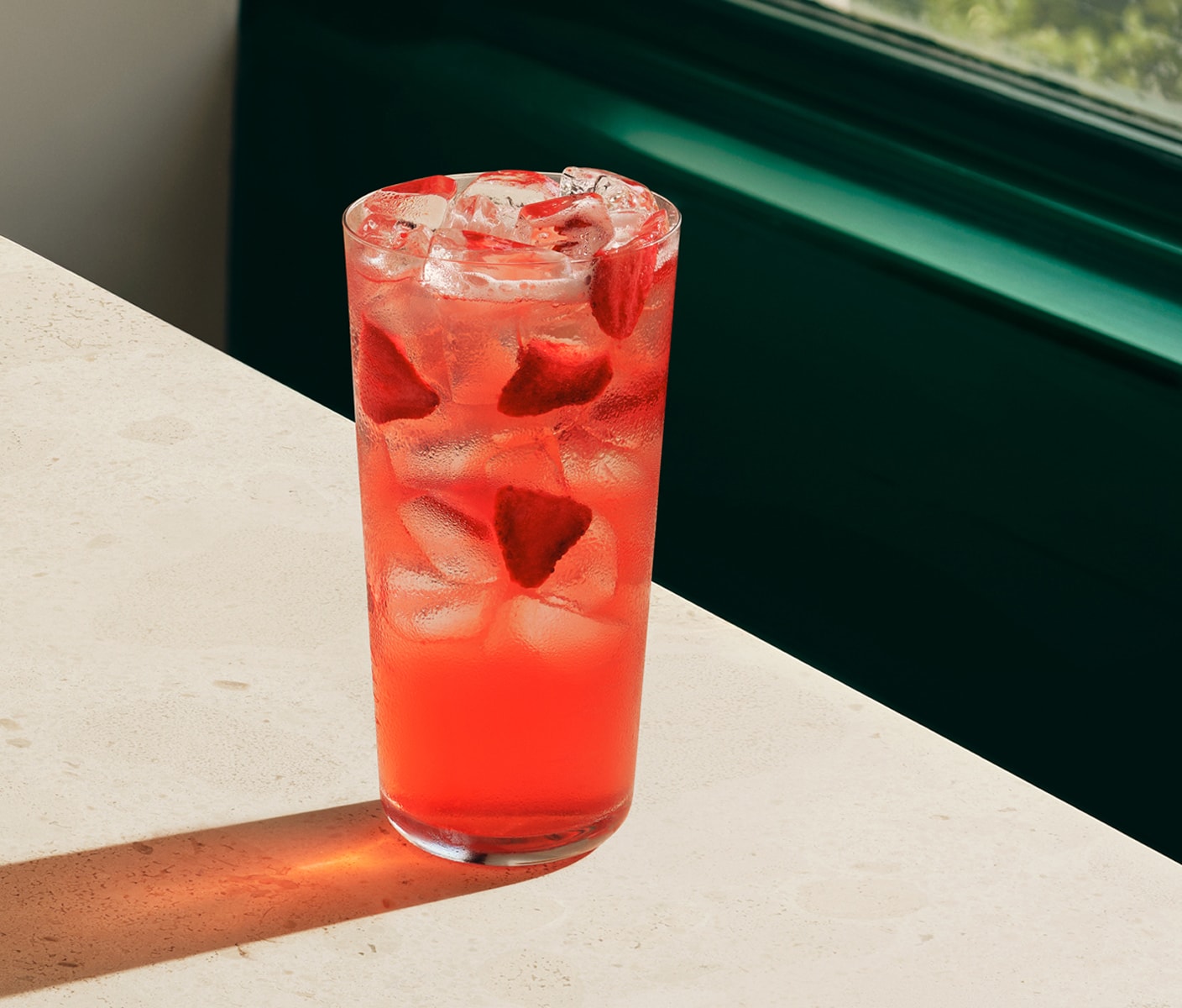 A bright iced beverage with pieces of strawberries in a glass.