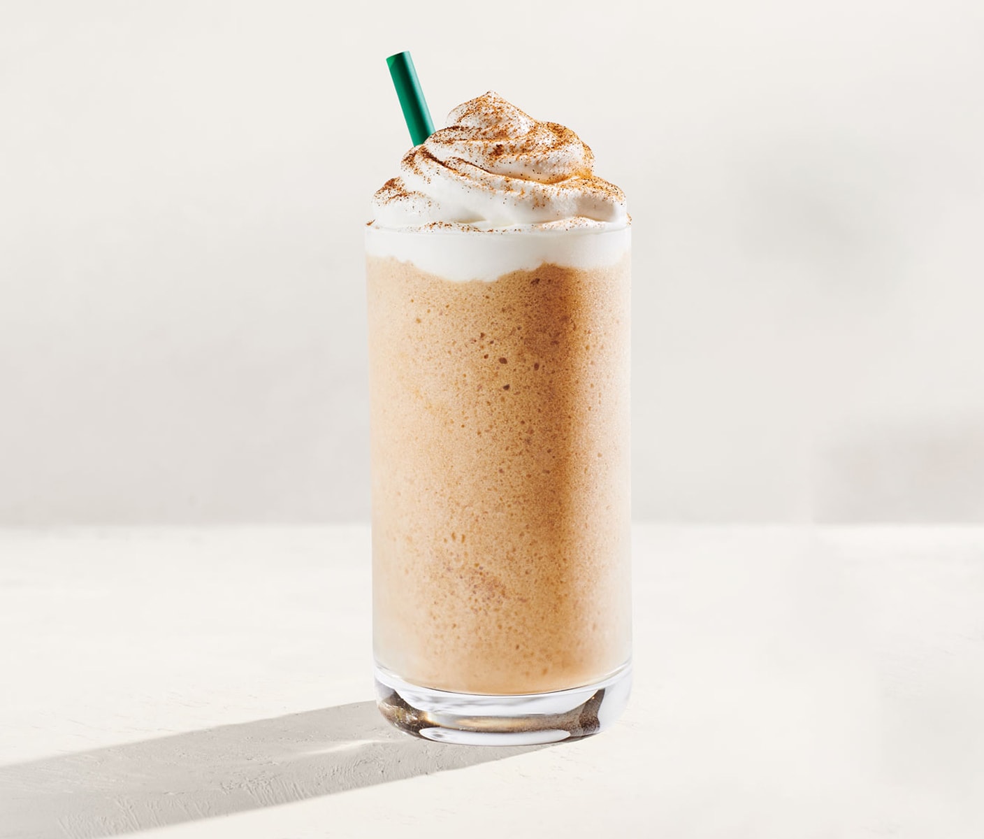 An blended iced coffee drink with whipped cream, sprinkles and a straw in a glass.