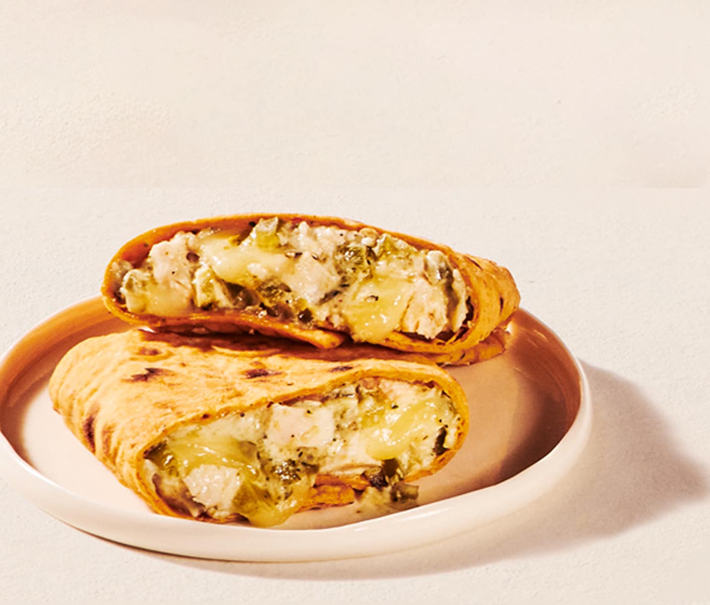 Two halves of a flatbrad wrap sandwich with a creamy chicken filling are stacked on a plate.