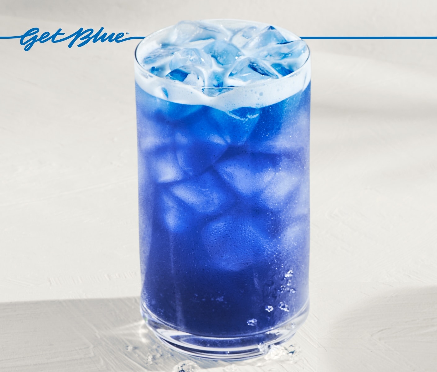 An iced blue drink in glassware on a light-gray surface. Blue script that reads “Get Blue” sits above it.