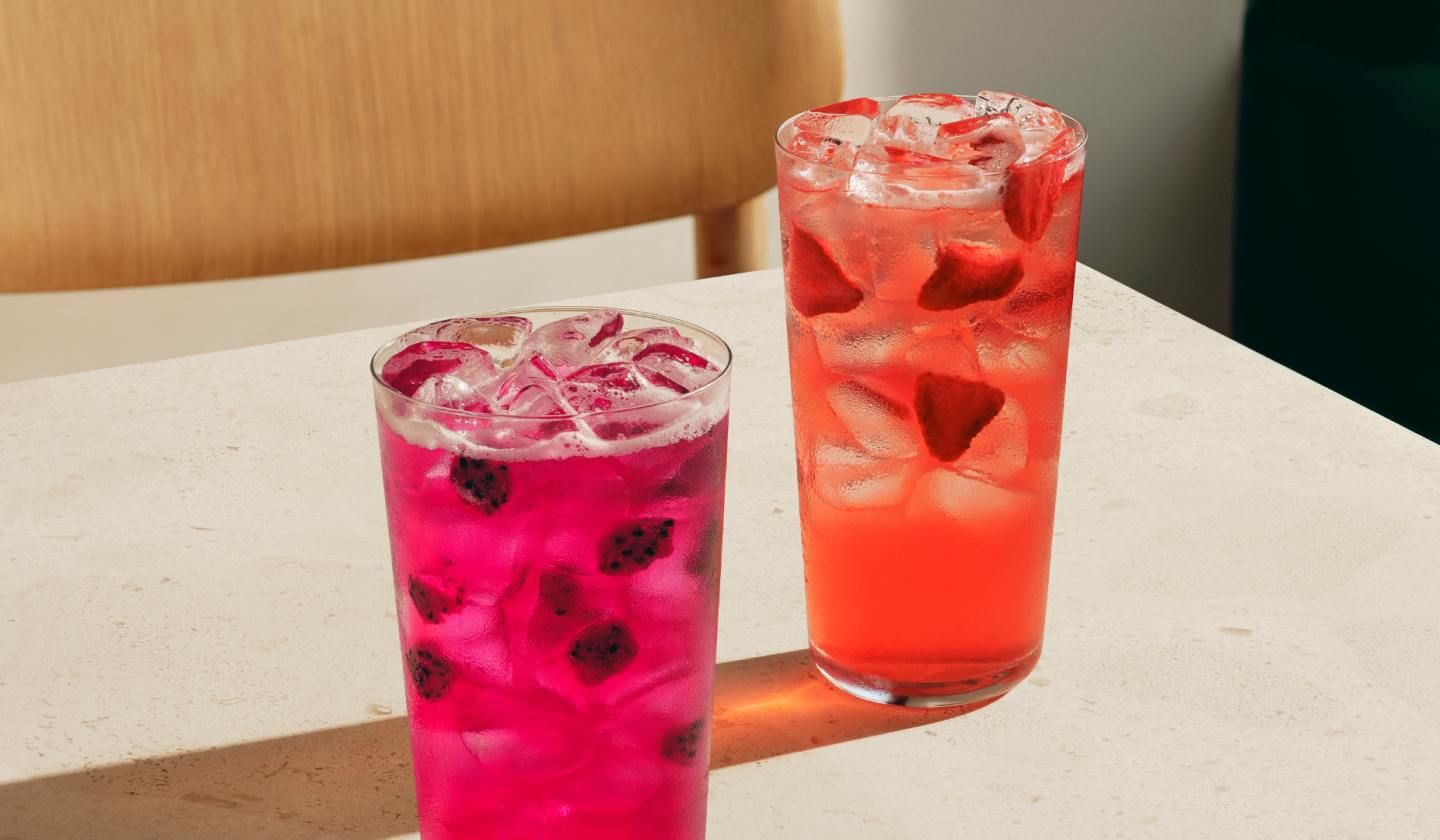 A Mango Dragonfruit Lemonade Energy Refresher and a Strawberry Açaí Energy Refresher on a café table.