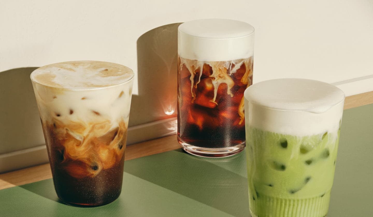 Two iced coffee drinks and one iced tea drink—all with thick foamy toppings in glasses.