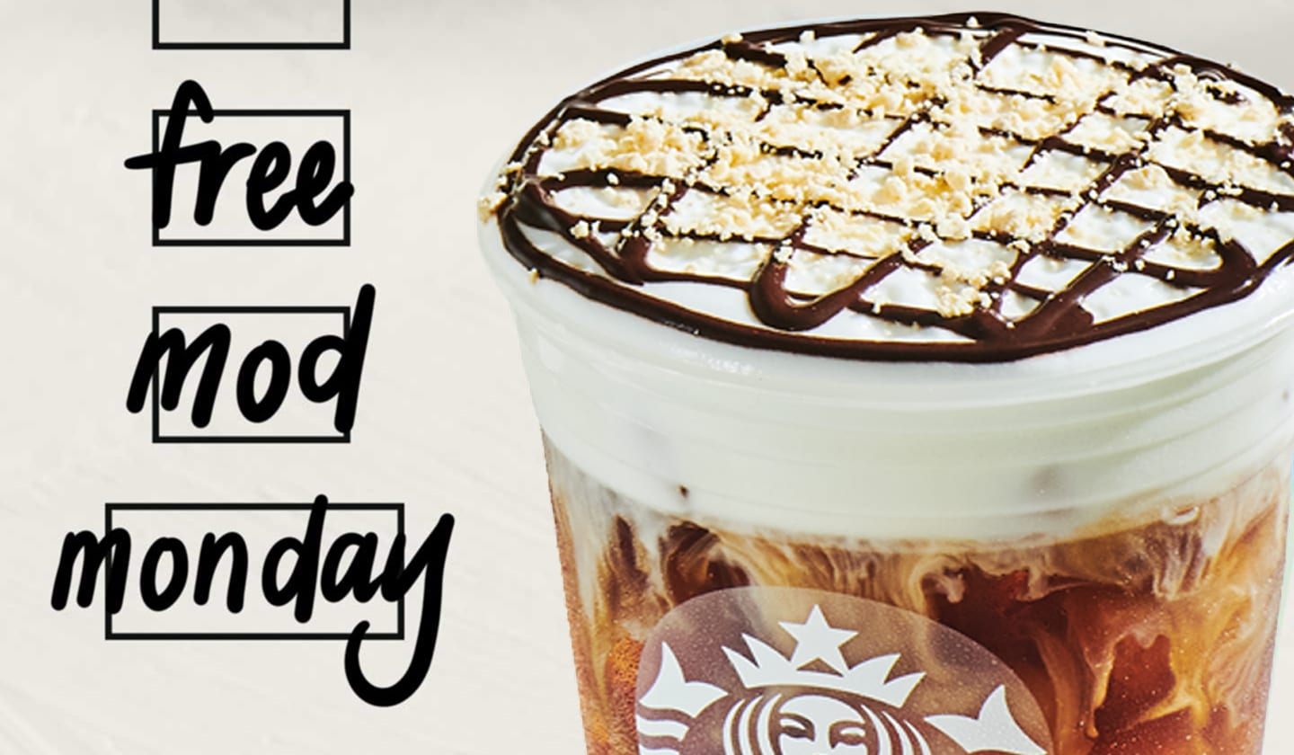 Close-up of an iced coffee drink topped with cold foam, mocha drizzle and sprinkles. To the left of the drink, three customization box icons have “Free,” “Mod” and “Monday” handwritten inside them in Sharpie.
