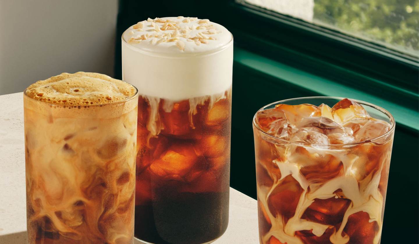 Three cold coffee drinks in glasses on a café table by a window.