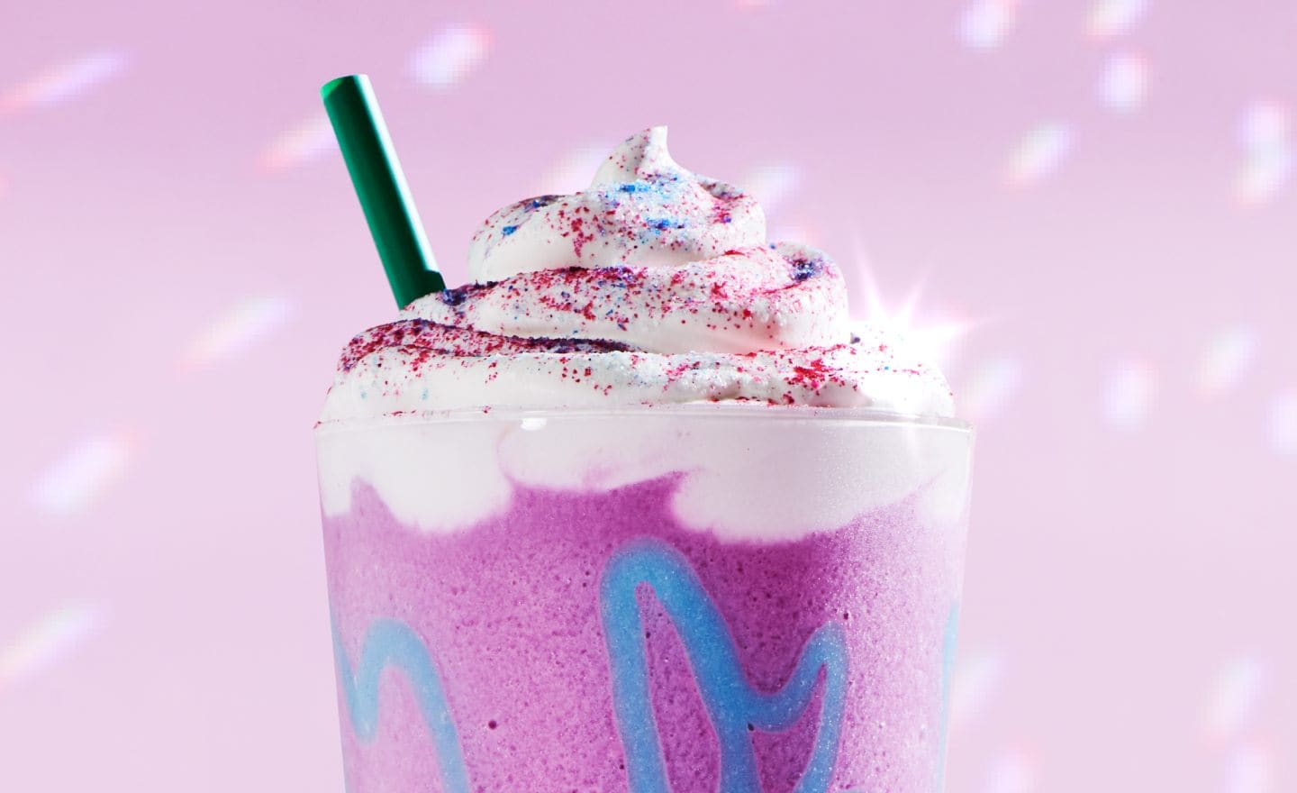 A Unicorn Frappuccino sparkles in front of a background with light refractions, as if reflecting from a disco ball.