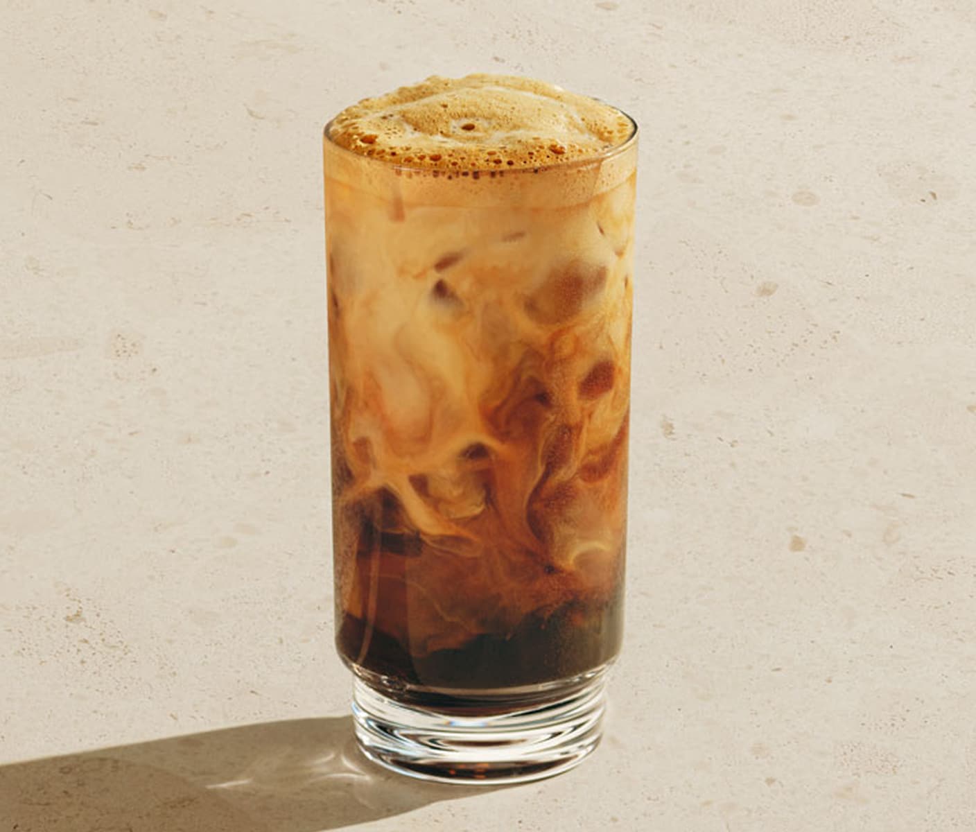 An iced coffee drink with a foamy top and marbling in a glass.