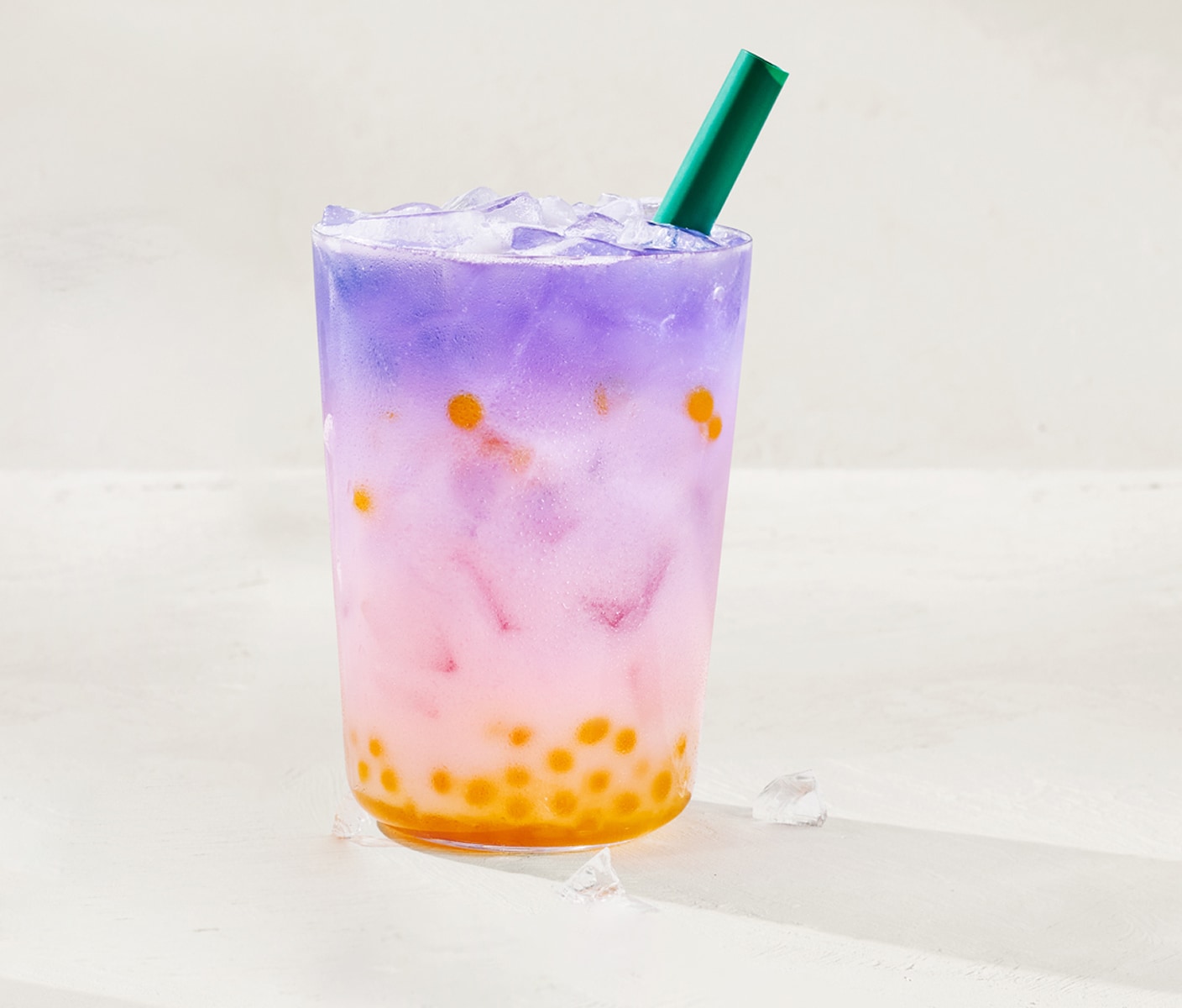A creamy multicolored iced beverage with round edible spheres at the bottom in a glass with a straw.