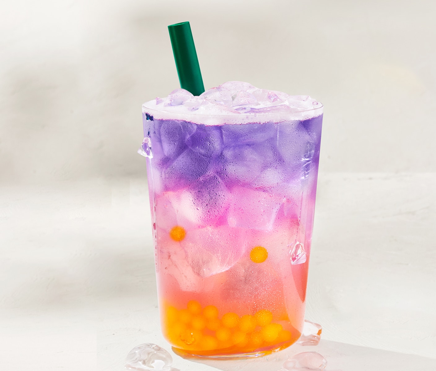 A bright multicolored iced beverage with round edible spheres at the bottom in a glass with a straw.