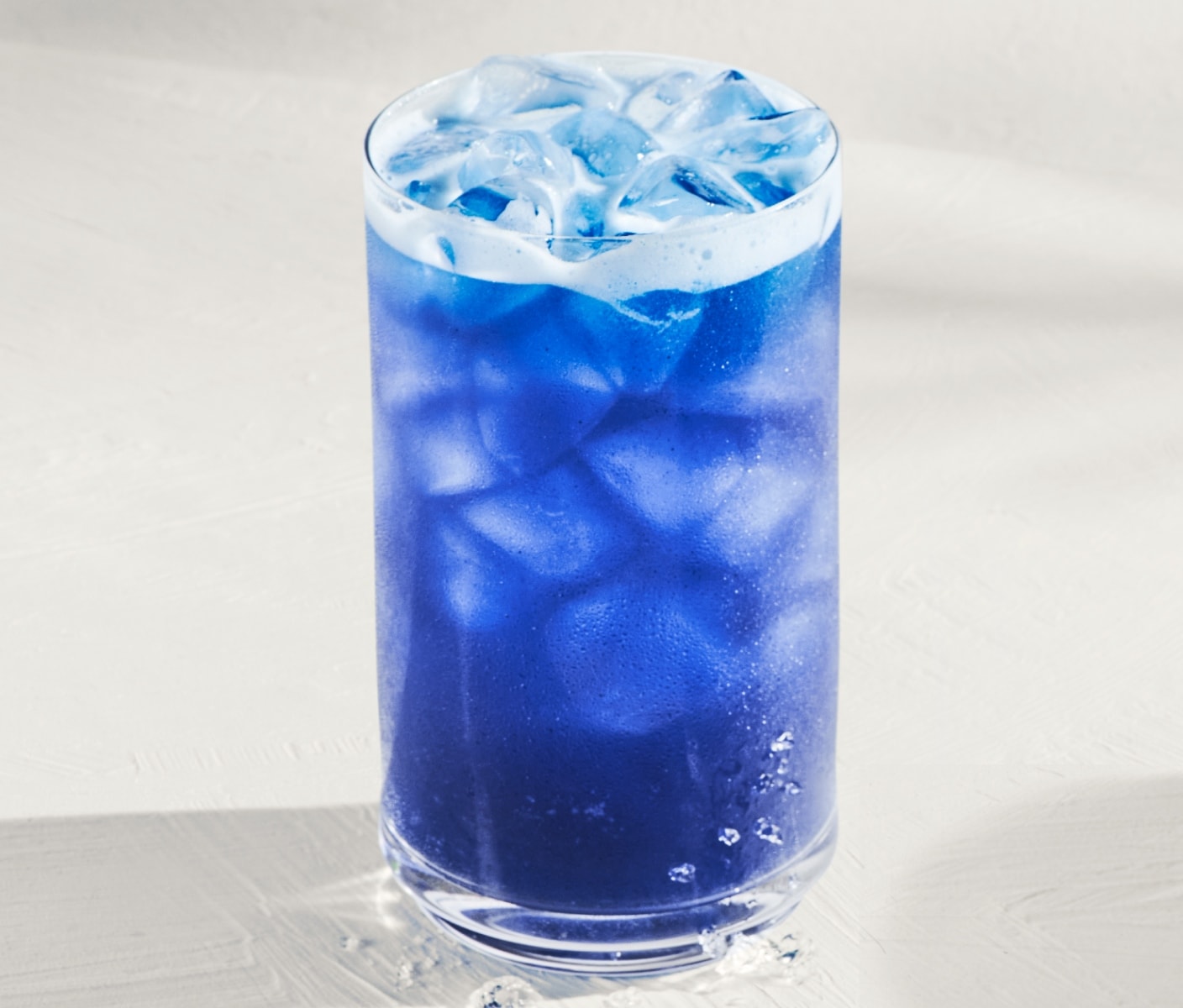 An iced blue drink in glassware on a light-gray surface.