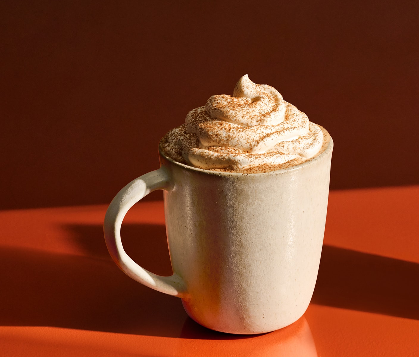 A hot drink topped with whipped cream and spices in a mug.