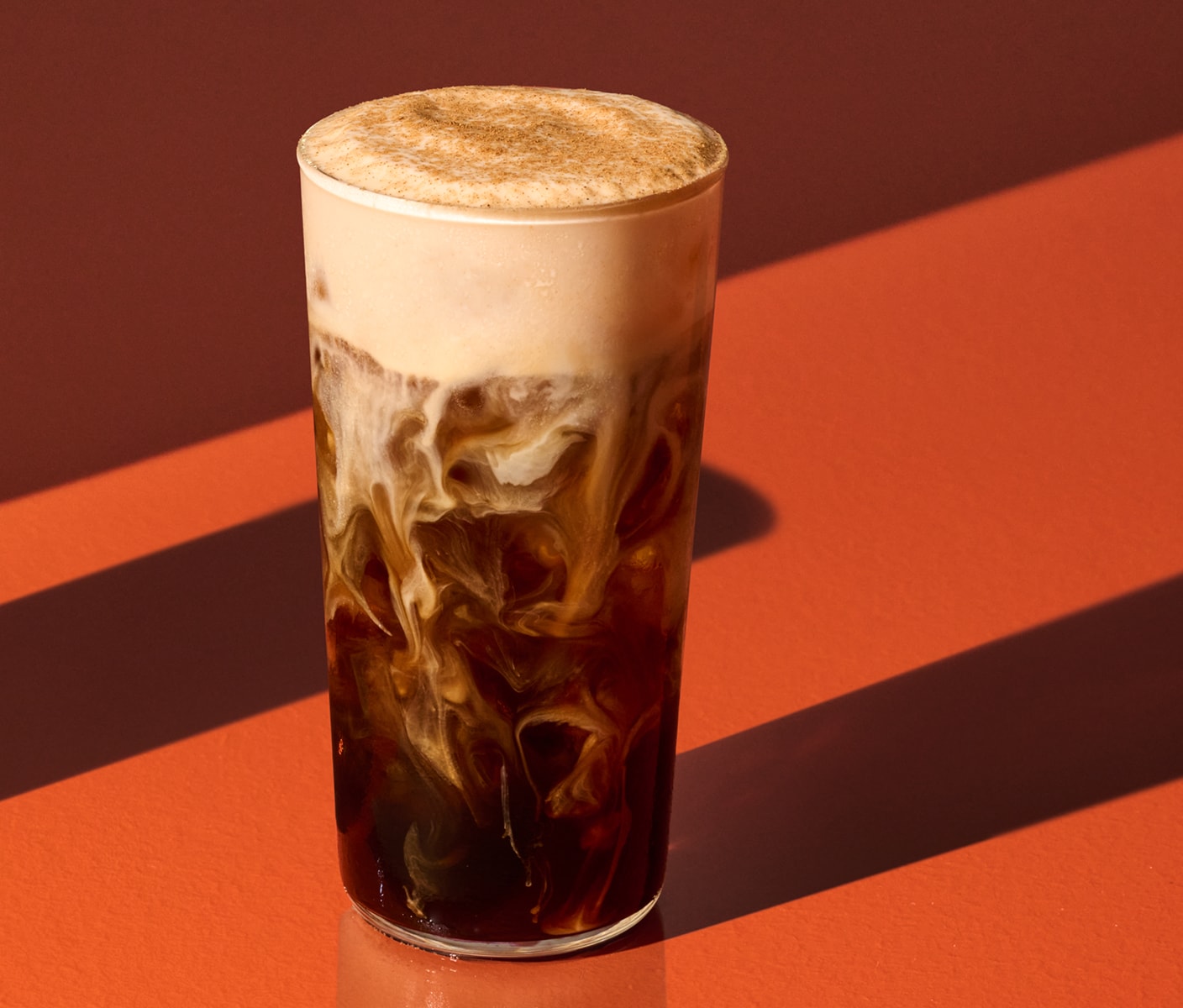 An iced coffee drink with creamy marbling topped with pumpkin cream cold foam and spices.