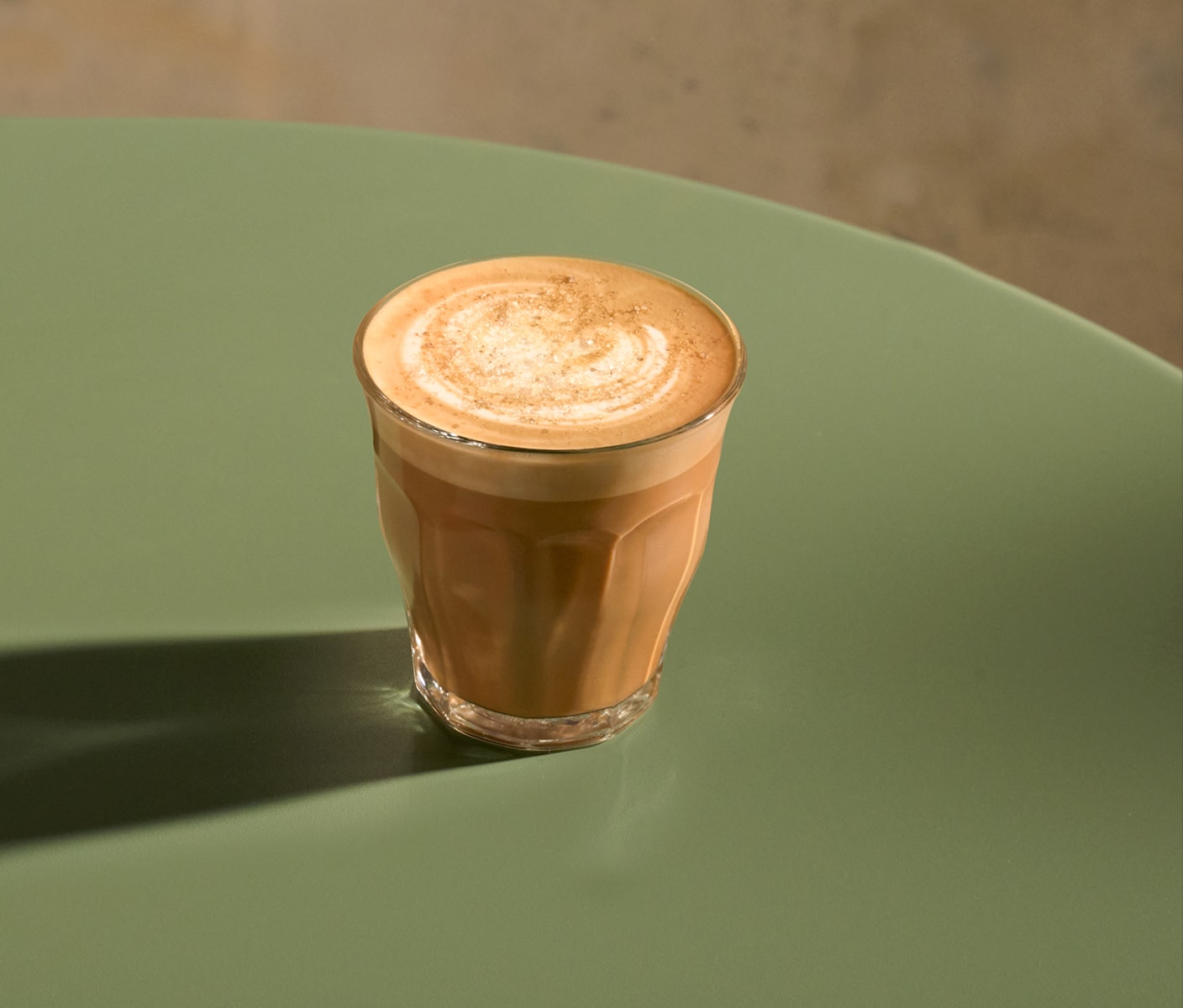 A hot coffee drink with foam sprinkled with topping in a small glass.