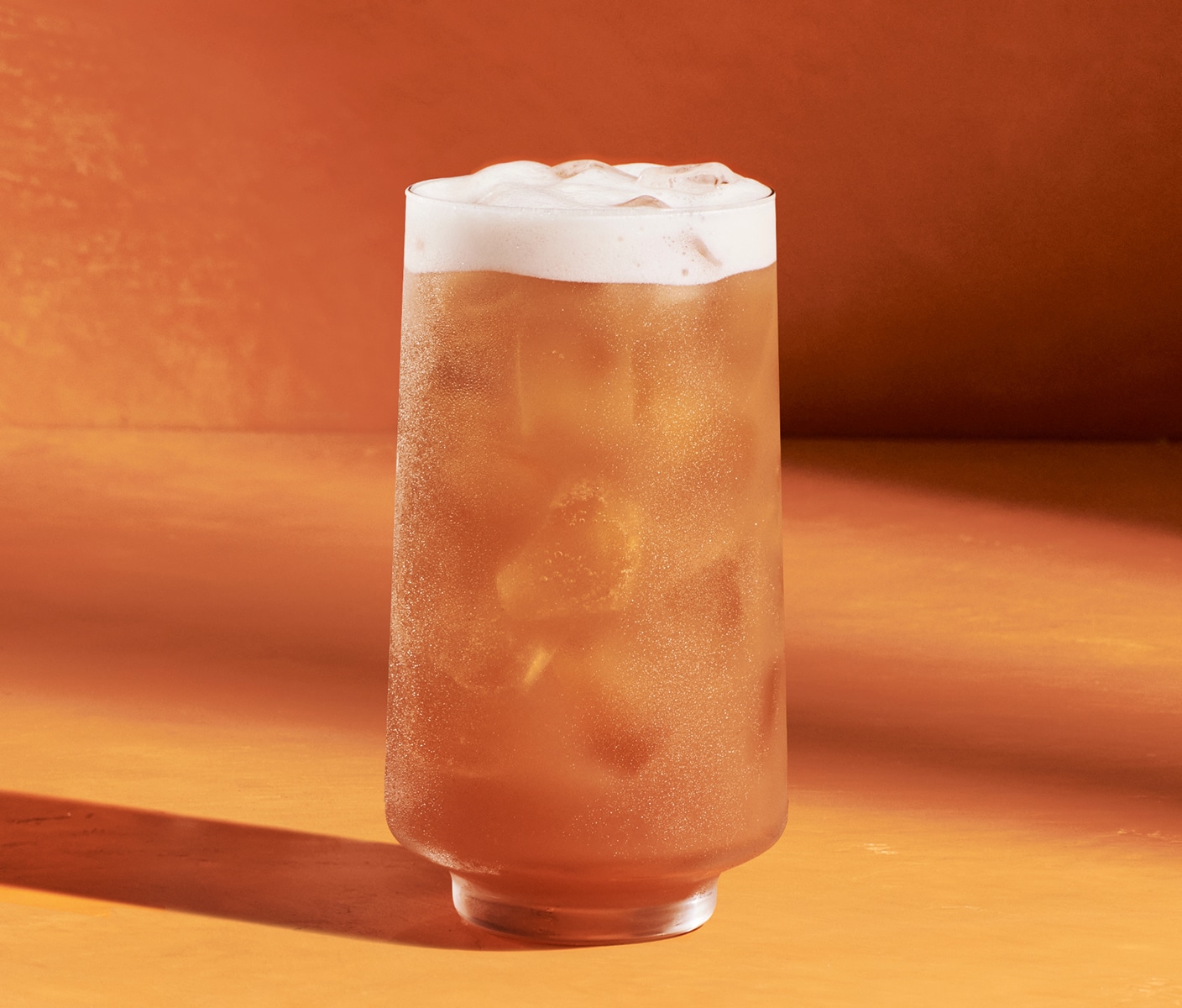 An iced orange drink with a layer of foam in a glass.
