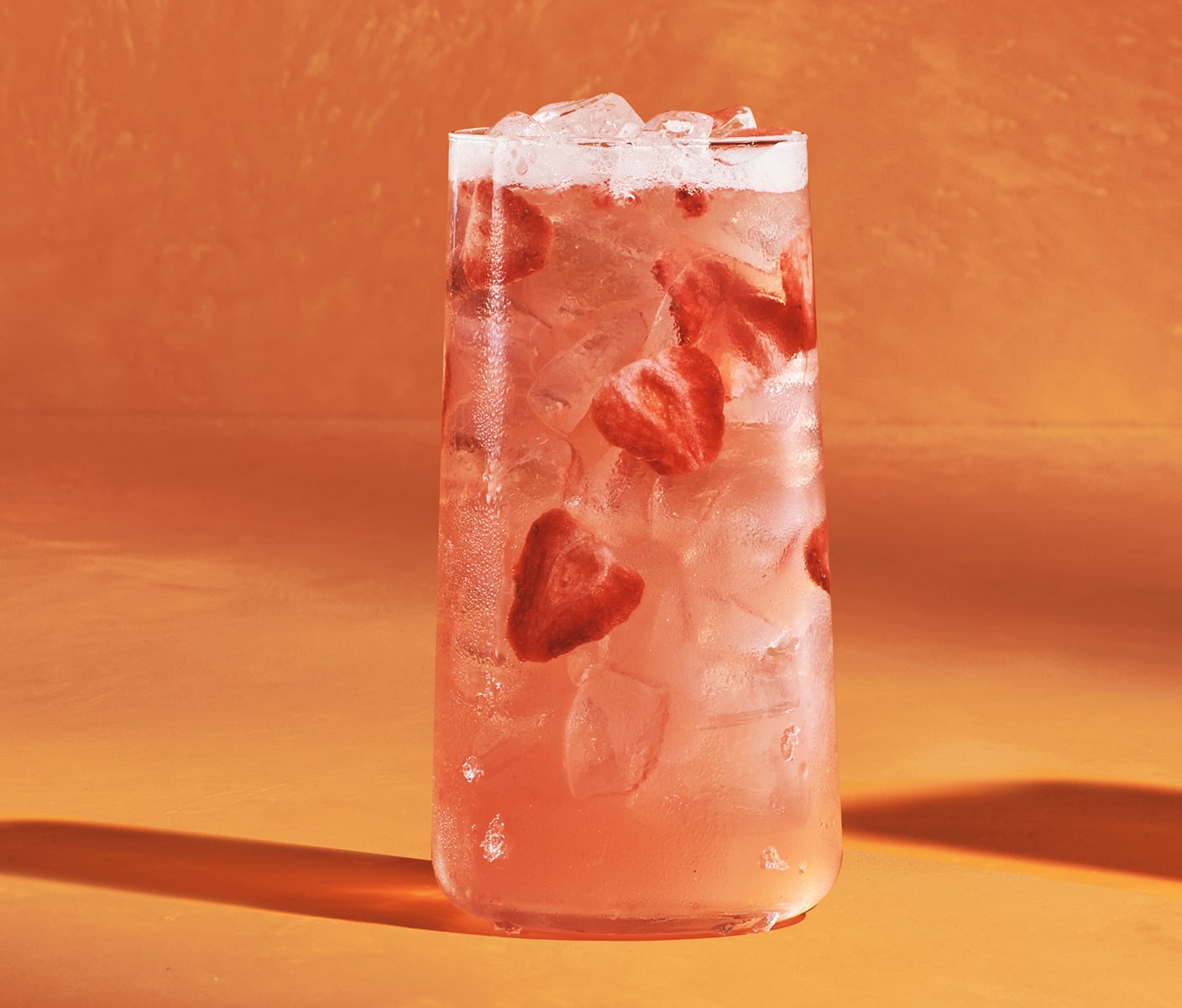 An iced pink drink with strawberry pieces in a glass.