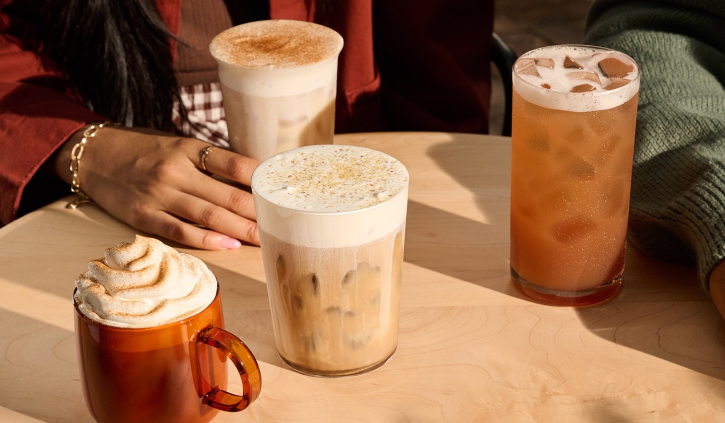 Four fall drinks on a table with hints of people gathered around them.