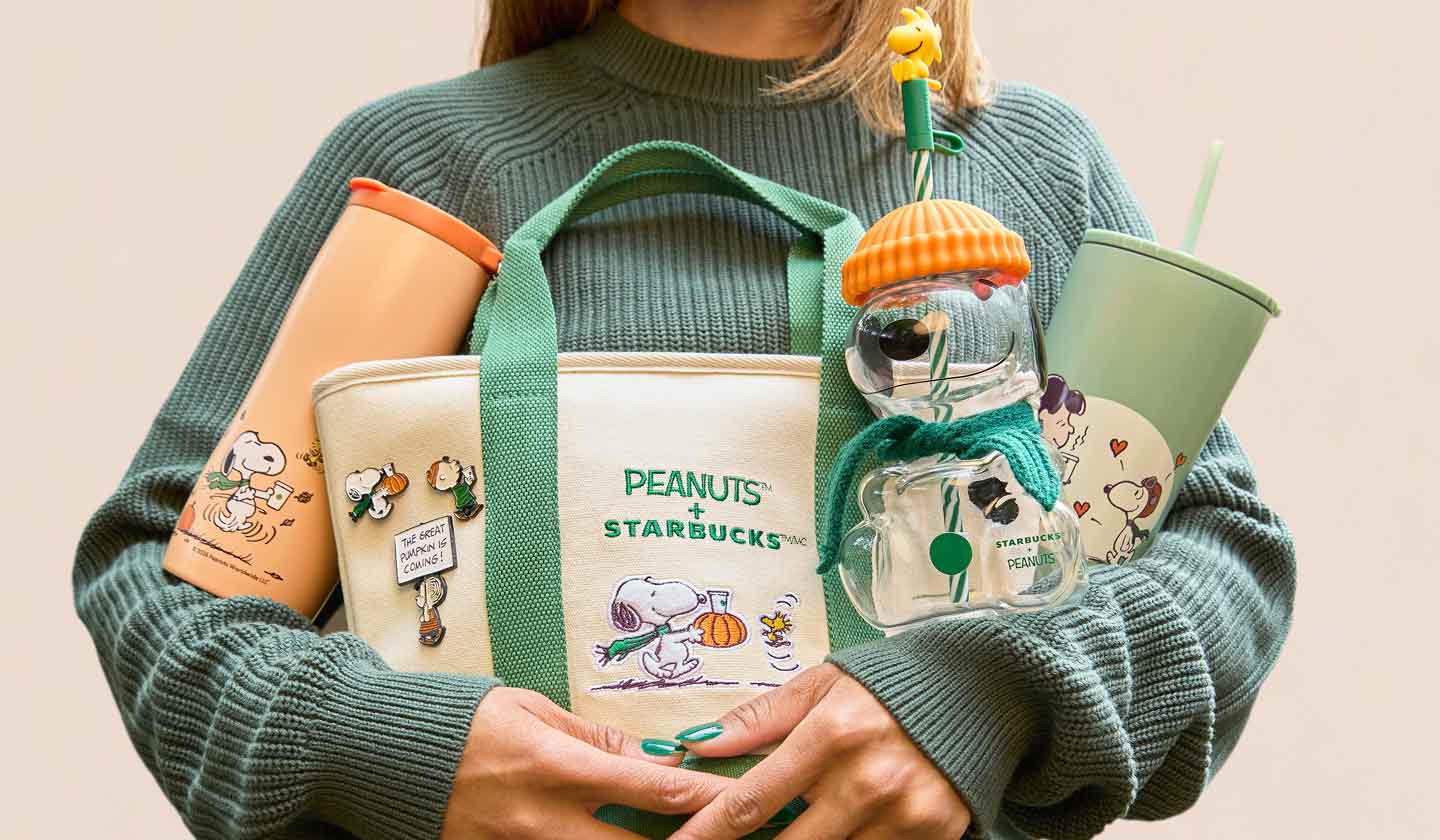 Someone in a knit sweater holding an armful of Peanuts™ and Starbucks branded merch.