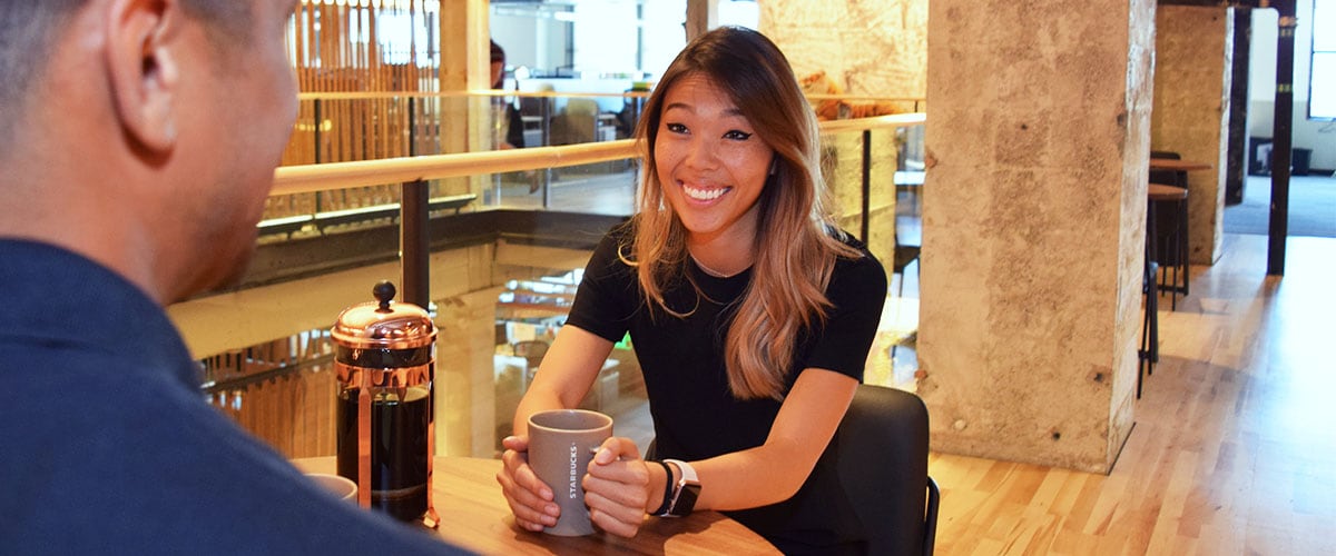 Woman seated at table holding coffee mug during interview