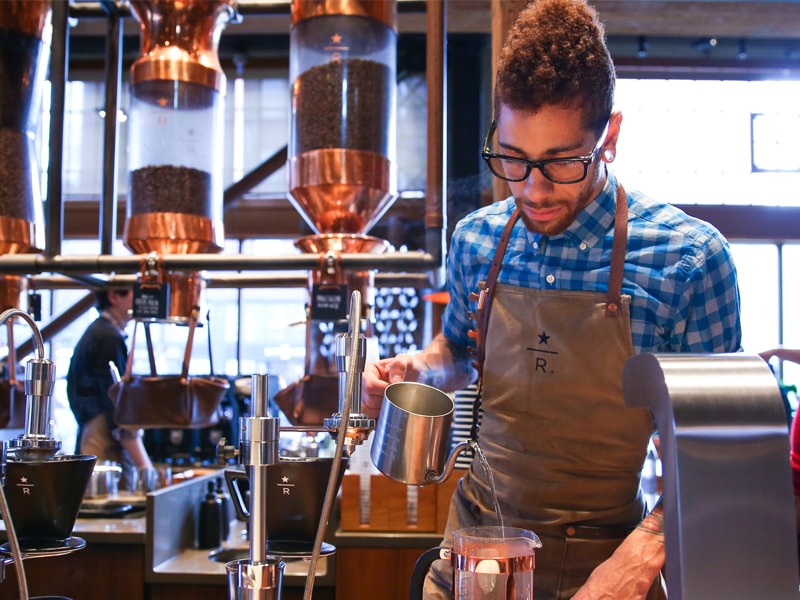 male partner at roastery pouring hot water into french press