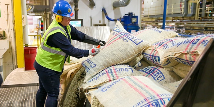 manufacturing partner wearing yellow safety vest, opening a burlap bag of coffee beans