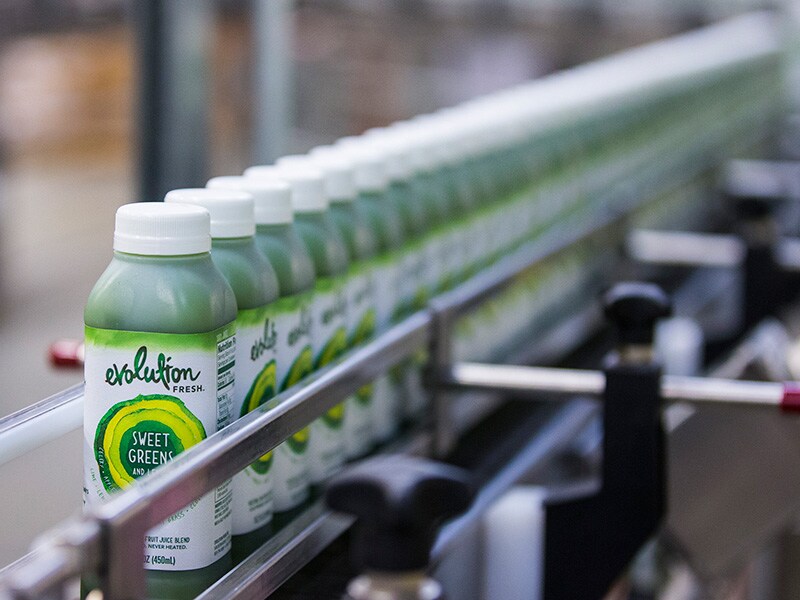 Long row of Evolution Fresh bottles of green juice moving through an assembly line