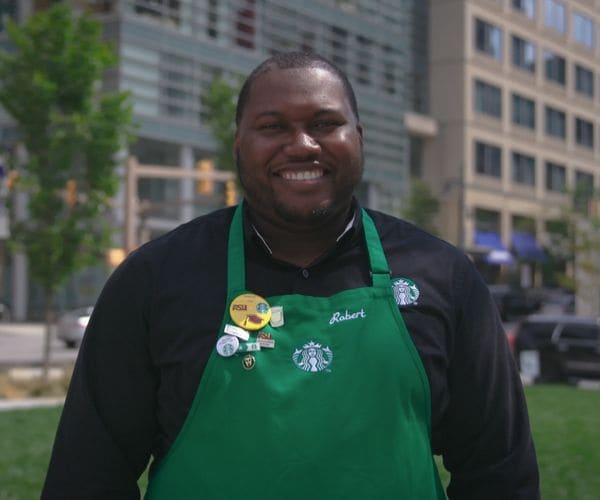 Diverse male employee smiling outside and wearing a green apron
