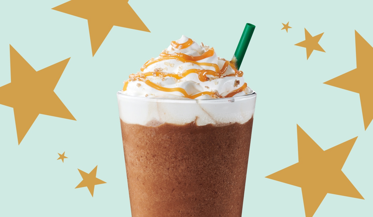 A blended Starbucks beverage topped with whipped cream sits on a pattern of gold stars atop a mint green background.