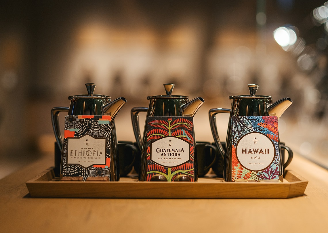 3 beautiful packages of coffee in front of stylish coffee pots.