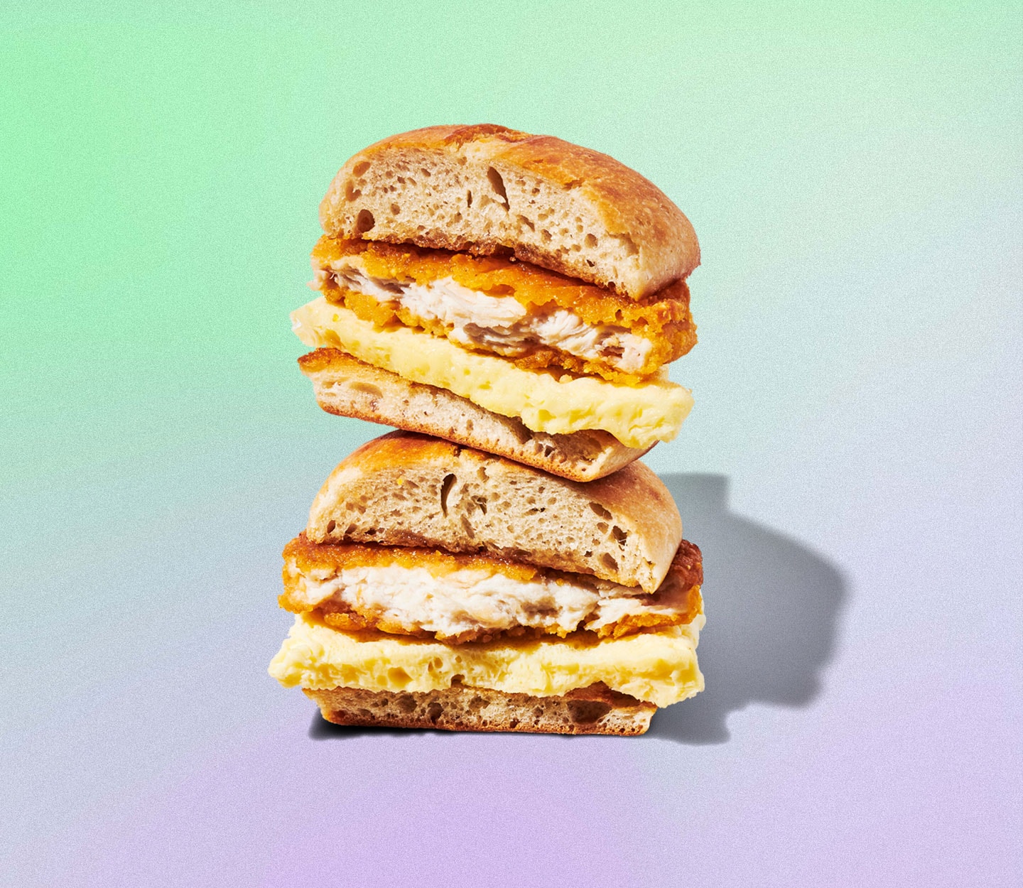 A Starbucks Chicken, Maple Butter & Egg Sandwich that is sliced in half and stacked on a cheerful background.