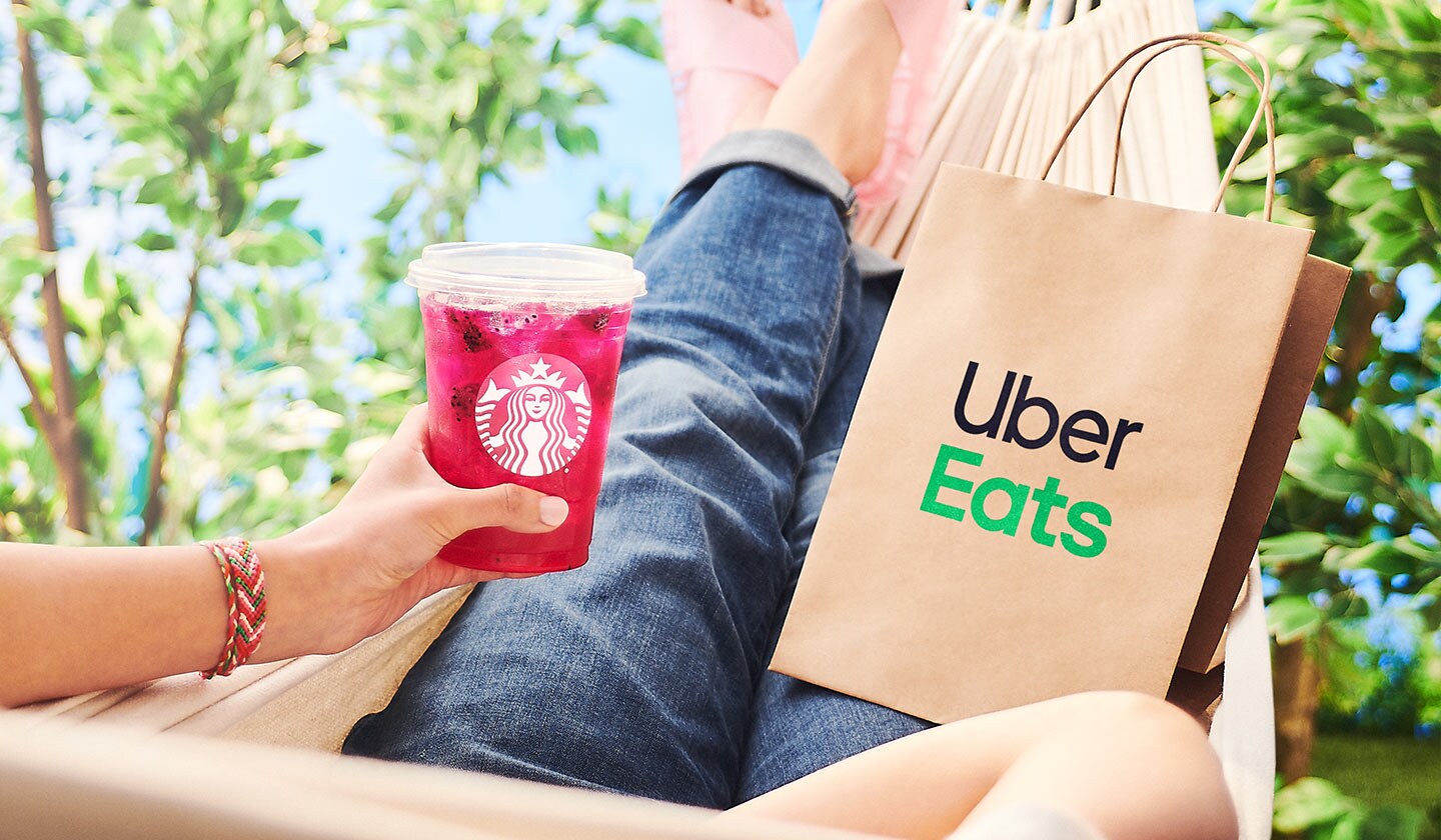 A person sitting in a hammock with a Starbucks drink and an Uber Eats delivery bag.