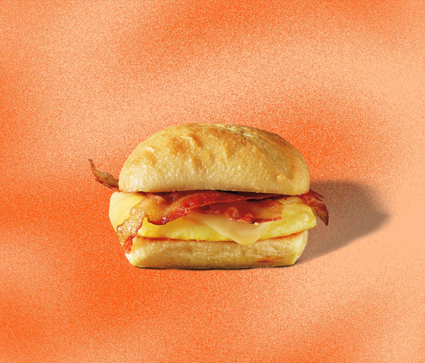 Side angle of a sandwich showing eggs, bacon and cheese between a fluffy bun.