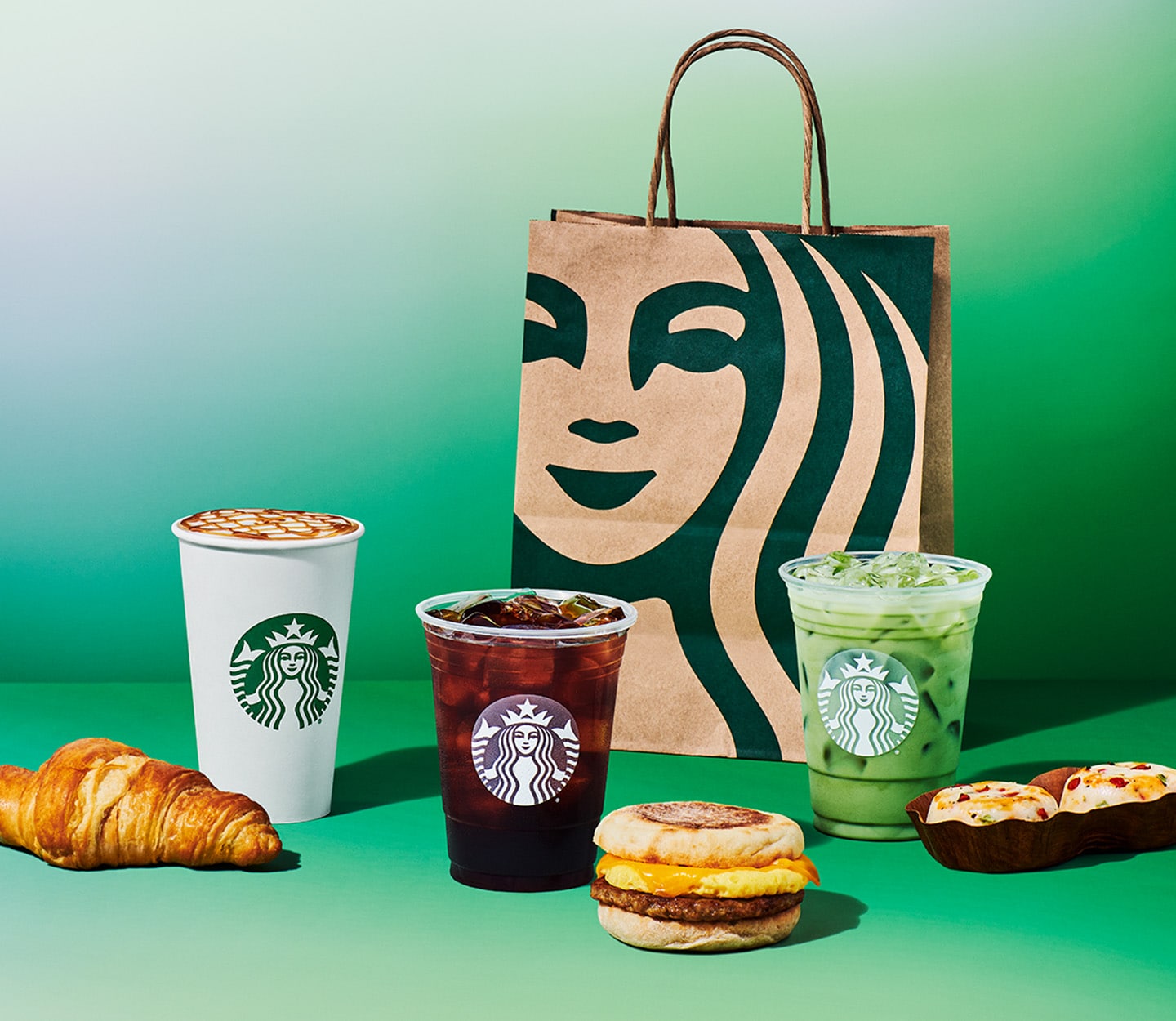 Starbucks drinks and breakfast food beside a Starbucks bag on a green background