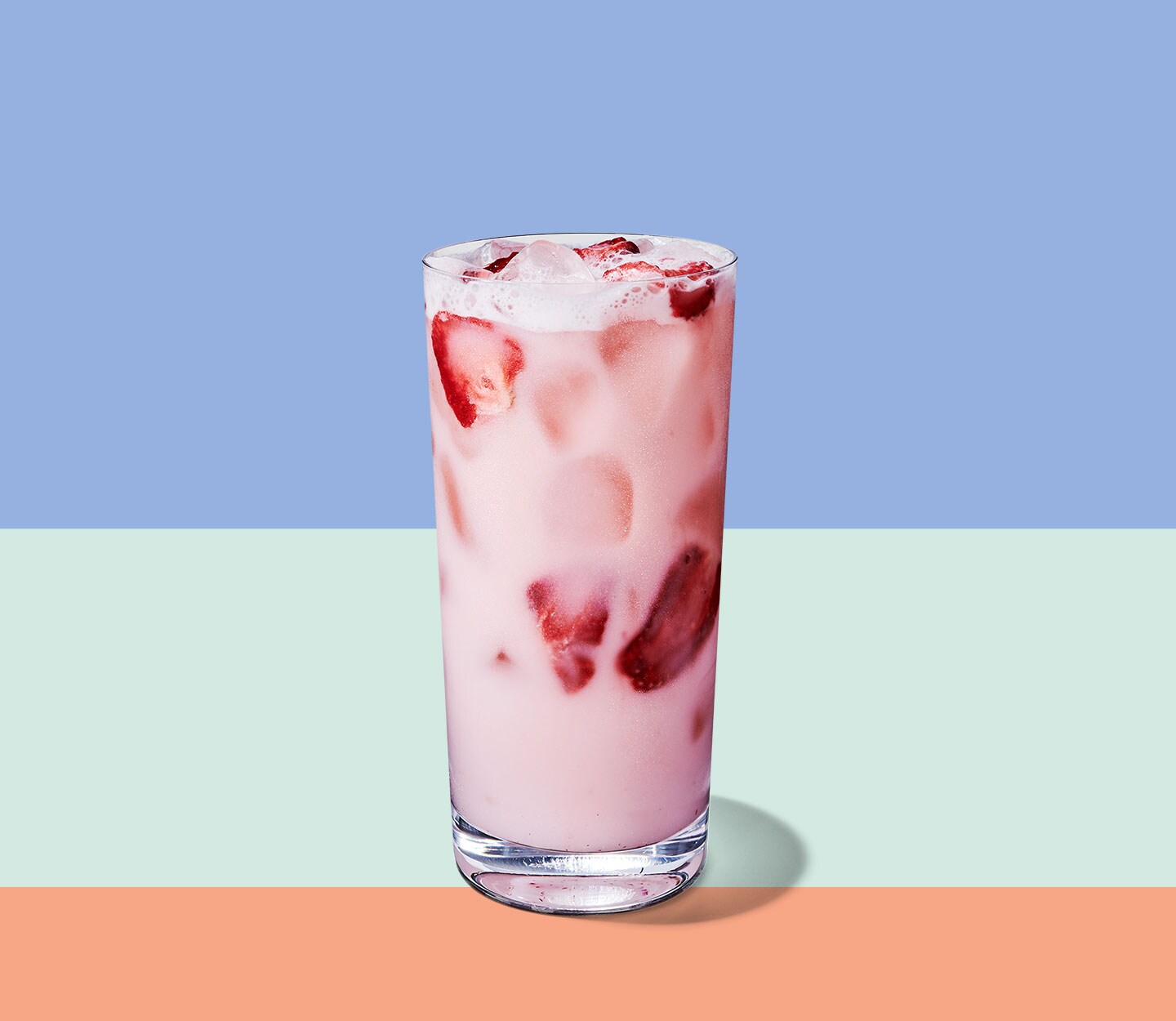 A cold, creamy drink in a tall, thin glass with strawberries floating throughout.