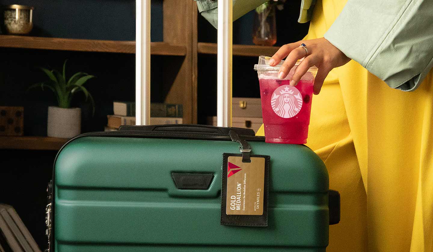 Woman with green suitcase holding a Mango Dragonfruit Starbucks Refreshers drink