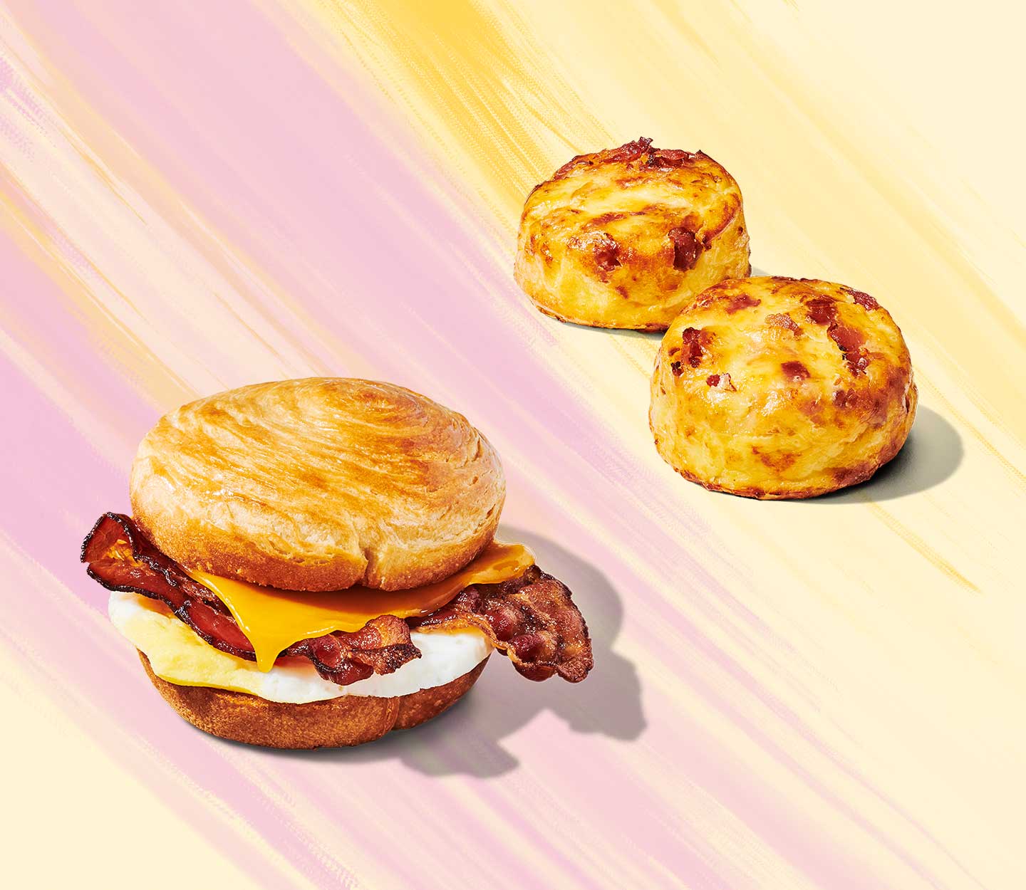 Bacon, cheese and egg sandwiched in a bun next to two round, fluffy egg bites.