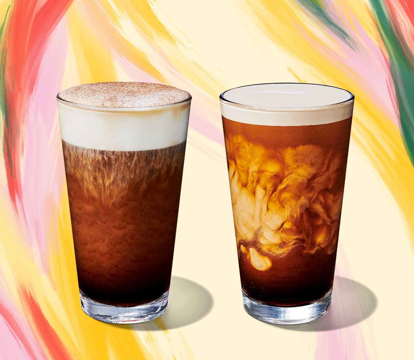 Cold coffee drink with foam topping next to a cold coffee drink with swirls of cream in tall glasses.