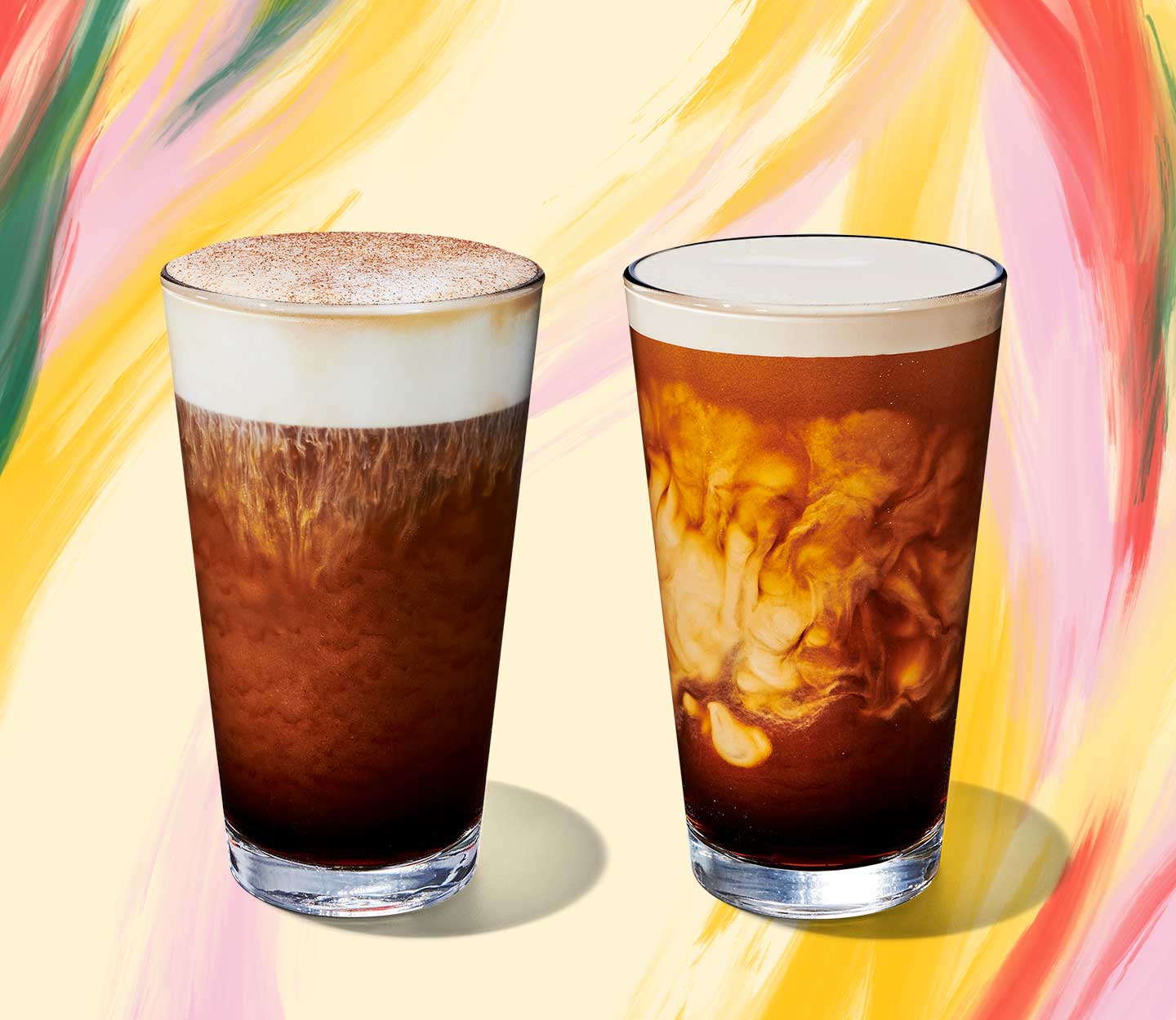 Cold coffee drink with foam topping next to a cold coffee drink with swirls of cream in tall glasses.