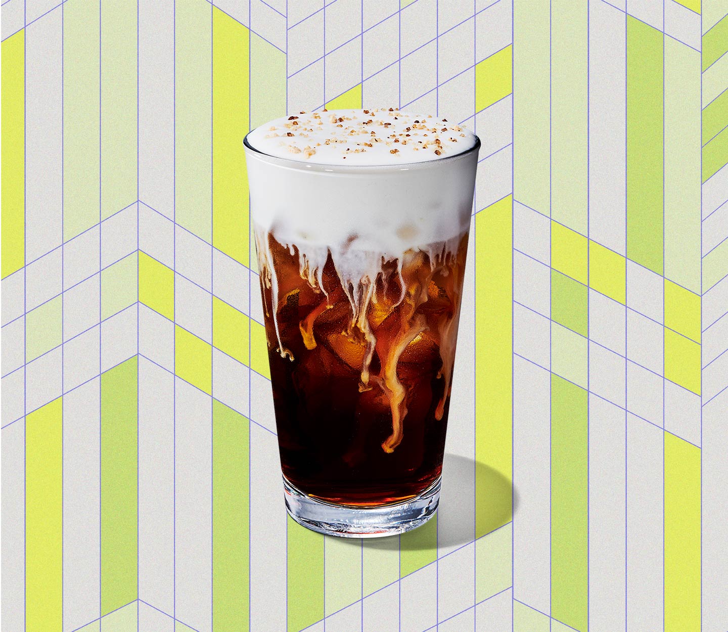Coffee in a tall glass with marbling throughout and a thick layer of foam with cookie sprinkles on top.