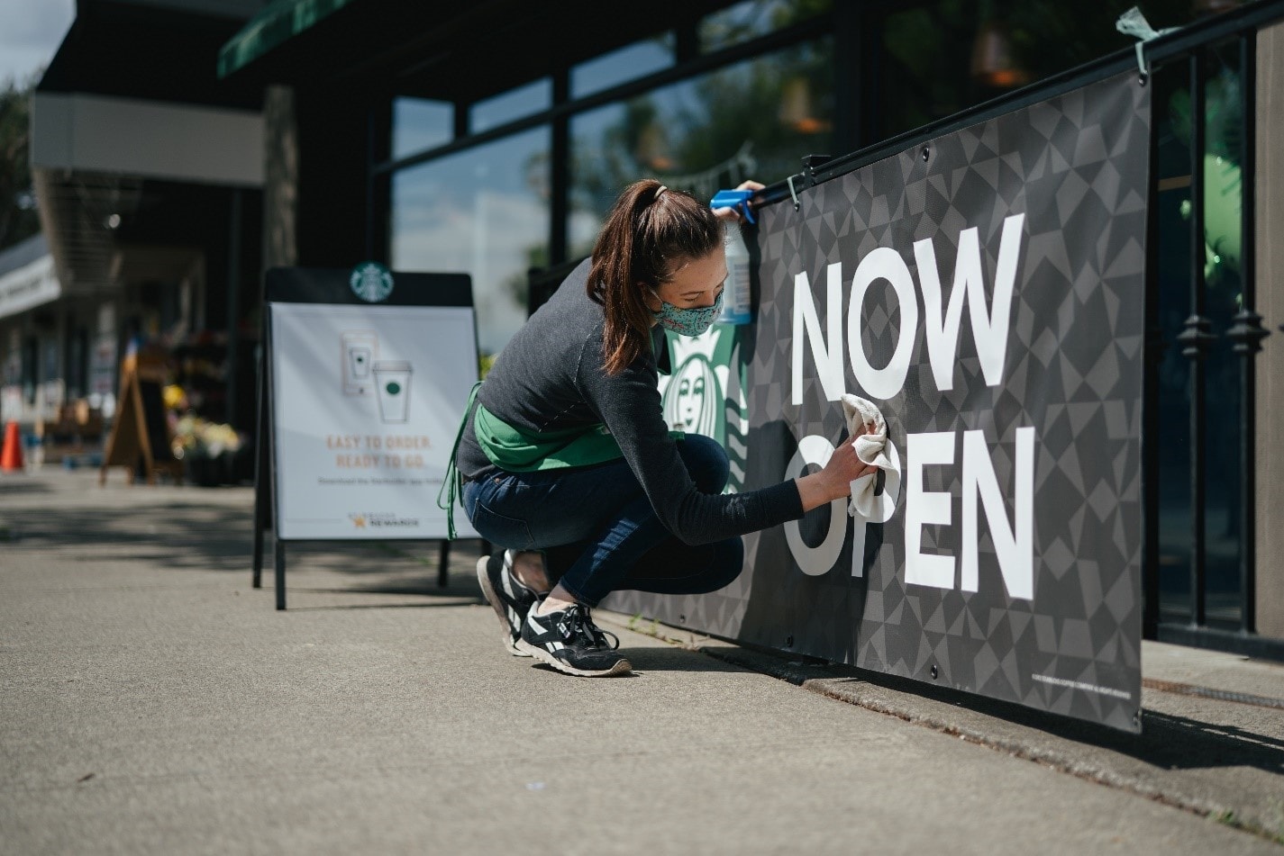 Starbucks employee wiping down a now open sign outside a Starbucks store