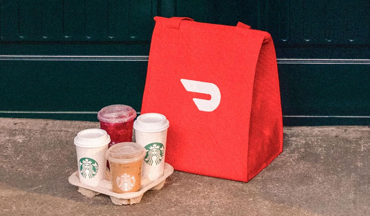 A red DoorDash delivery bag and Starbucks drink carrier filled with drinks sit on the front step of someones house.