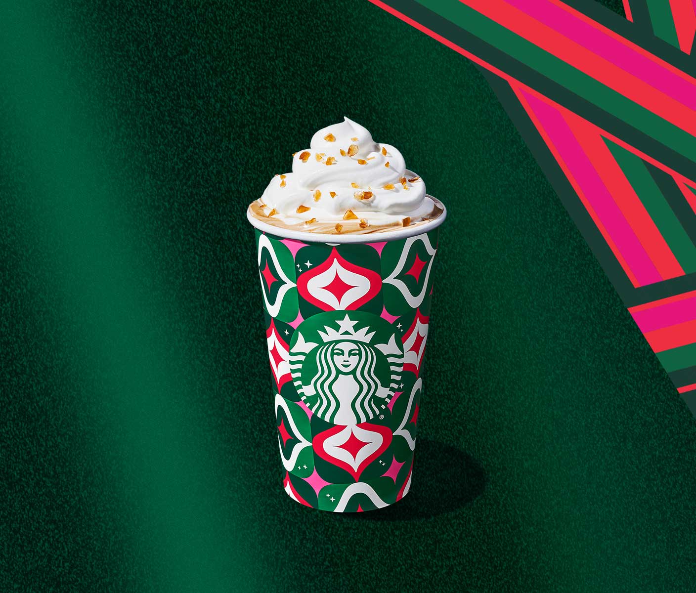 Hot espresso drink with whipped cream and caramel bits in a holiday-themed to-go cup.